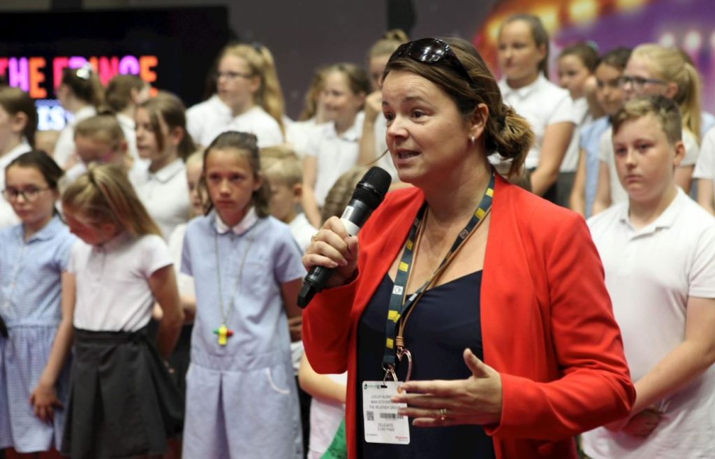 Person speaking into microphone at event with children on stage